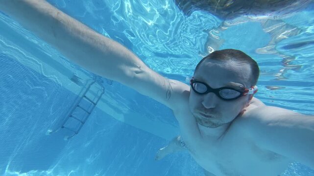 A person swims underwater in a pool while wearing goggles. The swimmer performs different poses and enjoys the water. The setting is bright and clear.