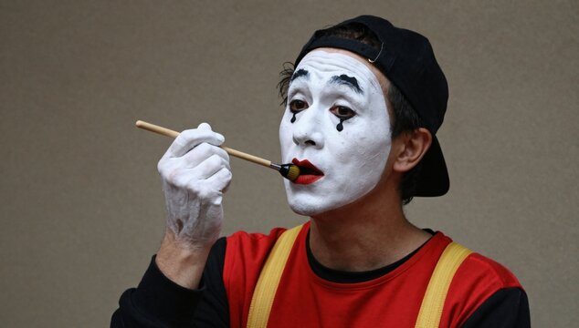 Male mime artist carefully applies bright red lipstick with a makeup brush in preparation for a performance