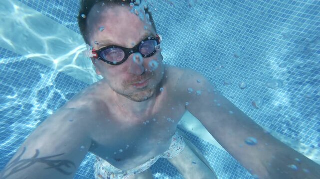 A man swims underwater in a clear pool, showing his playful side through different angles. Bubbles surround him as he enjoys his time in the water.