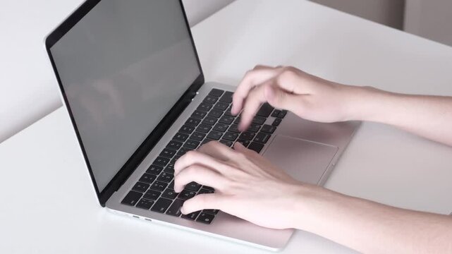 Hands typing on open laptop with blank bright screen in minimalist workspace, showing steady keyboard use on white desk with soft neutral light, clean modern composition for office tasks and online