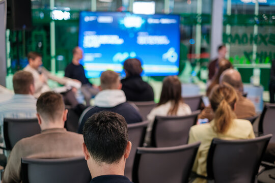 Business audience seated watching blurred presentation screen at conference, networking, learning atmosphere, modern meeting space.