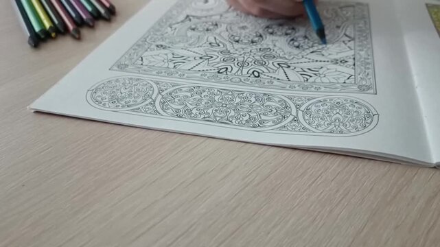 Overhead view of an open adult coloring book with intricate mandala patterns on a wooden table, colored pencils resting nearby.