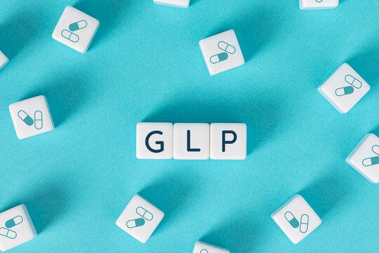 GLP word on blocks surrounded by medicine capsule icons on blue background