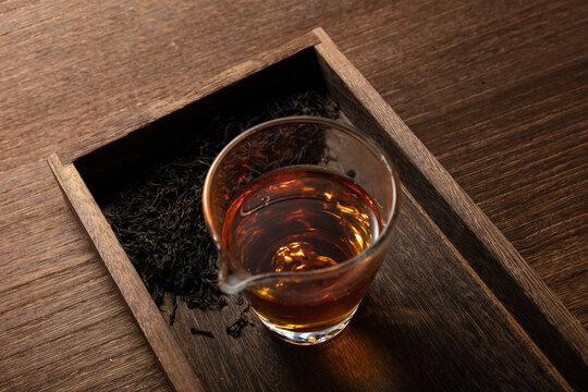 High angle view of a glass of freshly brewed black tea with dry loose leaves in a wooden tray on a rustic wooden table
