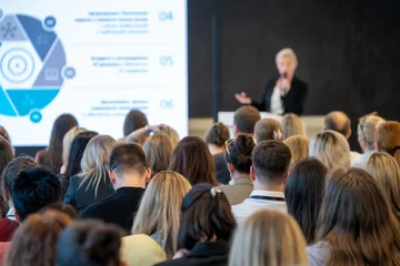 Presenter delivers slide based lecture to diverse audience, professionals listening attentively in conference room setting. © Anton Gvozdikov