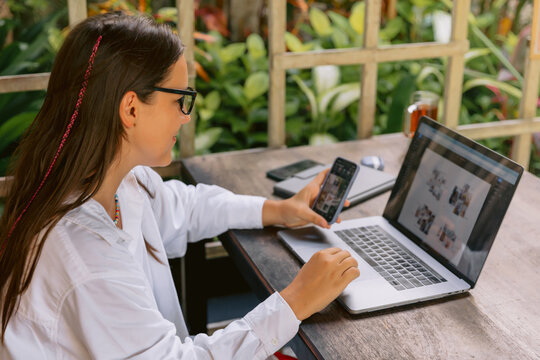 Woman working remotely with laptop and smartphone outdoors in tropical garden setting