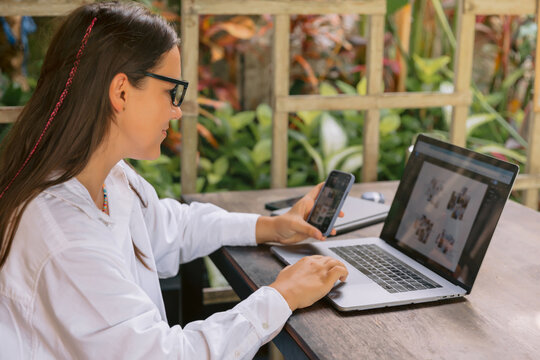 Woman using laptop and phone while working outside in green environment