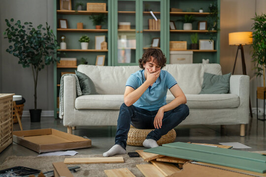 Young man frustrated assembling furniture in living room