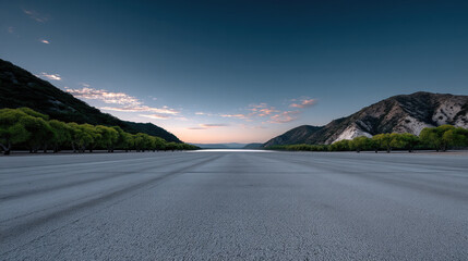 Obraz premium Empty asphalt surface with mountain landscape, green trees, blue sky, and soft sunrise light, peaceful and serene outdoor scene