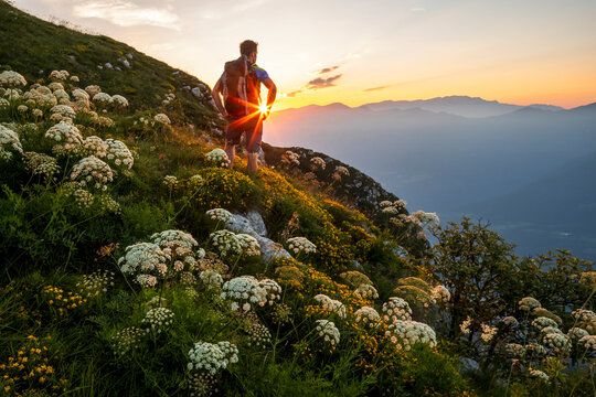 Hiker with backpack explores a wildflower mountain slope at sunset, capturing the spirit of outdoor travel and adventure in Monte Baldo Natural Park, Brentonico, Trentino, Veneto, Italy.