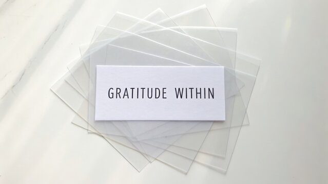 Inspirational Message of Gratitude on a Simple Card Surrounded by Clear Transparent Sheets on a White Surface