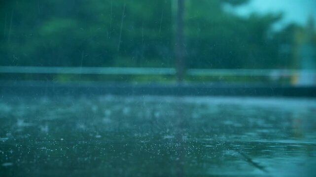 Heavy rainfall pouring on concrete floor with lush green foliage background