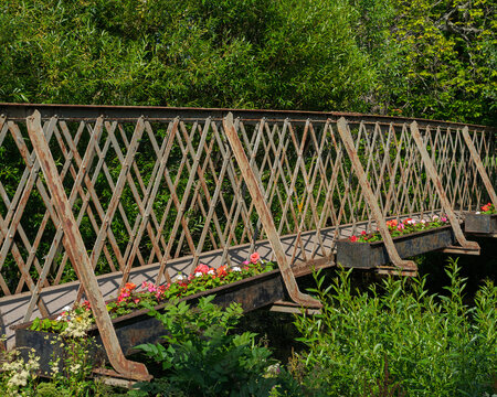 Historic iron footbridge crossing Mosset Burn in Forres, Moray, Scotland, decorated with bright flowers