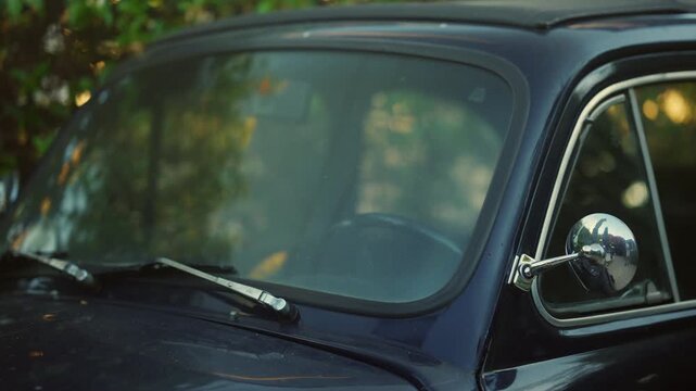Close up of a vintage dark blue classic car windshield and chrome side mirror