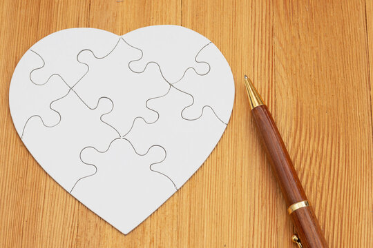 Blank white puzzle heart with a pen on a wood desk for divorce