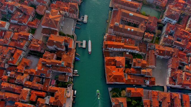 Top down aerial view of the Grand Canal in Venice, Italy, with a vaporetto water bus, work boats, a ferry pontoon, moored boats and terracotta rooftops lining both banks in spring.