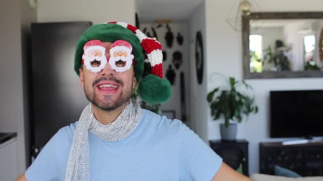 Man wearing Christmas hat and Santa Claus weird eyeglasses dancing at home