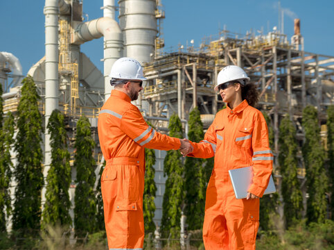 Professional male female engineer  jumpsuit shak hand front oil refinery infrastructure representing successful business partnership industrial agreement teamwork corporate achievement energy sector