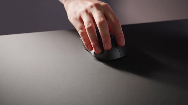A hand reaches out to a sleek black computer mouse on a dark desk, pulls away briefly, and then returns to grip it, showcasing minimalist design and smooth movement.