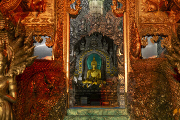 Obraz premium Golden Buddha statue framed by ornate silver and gold temple carvings and dragon guardians, warm light creating reverent and serene atmosphere in Thai silver temple interior