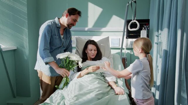 Father and daughter give flowers to mother in hospital ward
