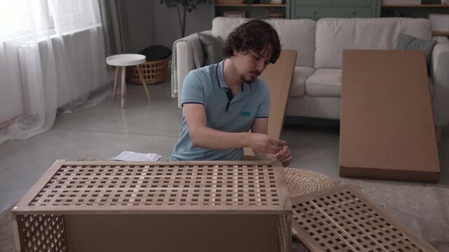 Young man assembling new wooden furniture at home