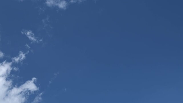 white fluffy clouds run fast across a bright blue sky on a sunny summer day