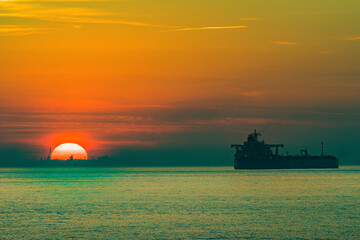 Cargo ship sailing at sunset in industrial port © Georges
