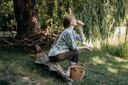 Woman drinking from reusable cup outdoors, enjoying simple moments, refreshing break, slow living, nature escape