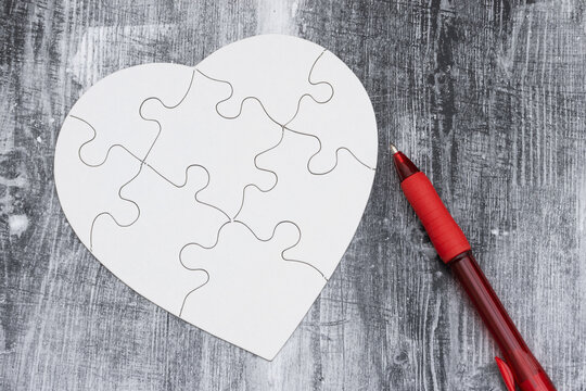 Blank white puzzle heart with pen on weathered wood for grief and loss
