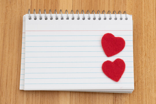 Blank spiral notebook of index cards with two red hearts on wood desk