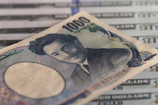 Close-up of Japanese 1000 yen banknote on top of US hundred dollar bills with selective focus