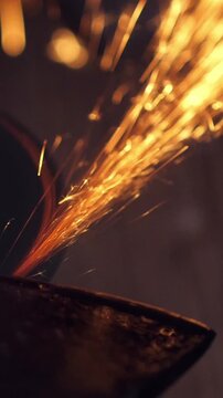 Man sharpen axe with grinder in the dark with flying sparks. Vertical footage