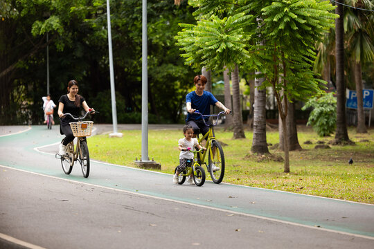 Happy Smiling father and mother with girl kid on bicycles having fun in city park. outdoor activitie with daughter father, mother and grandfather