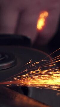 Man sharpen axe with grinder with flying sparks. Vertical footage