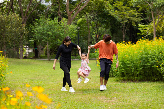 Mother and Father holding and jump up daughter in the air at spring park, moment of family bonding and togetherness. outdoor activitie. Asian Family with father mother daughter and grandfather
