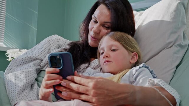 Mother embraces daughter while sharing smartphone in hospital