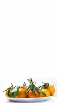 Pile of tangerines with green leaves on plate. Closeup. Rotating. Vertical footage