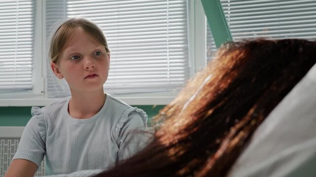 Girl speaks calmly with mother during hospital recovery in ward