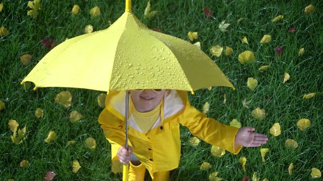 A happy child plays outside in an autumn park. A child with a yellow umbrella enjoys the autumn rain. Slow motion