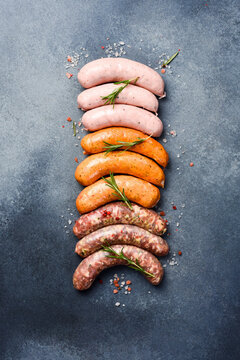 Uncooked mix of barbecue sausages: beef, pork and chicken sausages. On a gray concrete background. Top view.