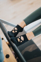 Close-up of a woman's feet wearing black pilates socks on a reformer bar. Footwork during a pilates reformer workout highlighting grip socks and athletic form.