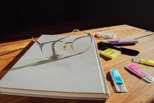 Glasses on a notebook on a wooden desk with stationery and exam notes