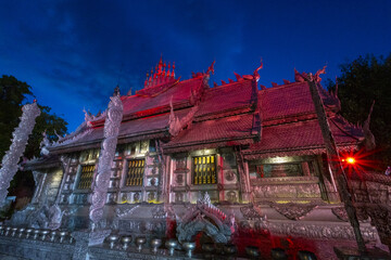 Obraz premium Silver temple exterior at dusk with ornate carved roof and reflective metal facade lit by colored lights creating dramatic atmosphere