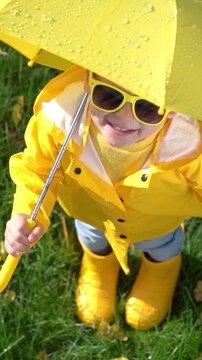 A happy child plays outside in an autumn park. A child with a yellow umbrella enjoys the autumn rain. Vertical video, slow motion