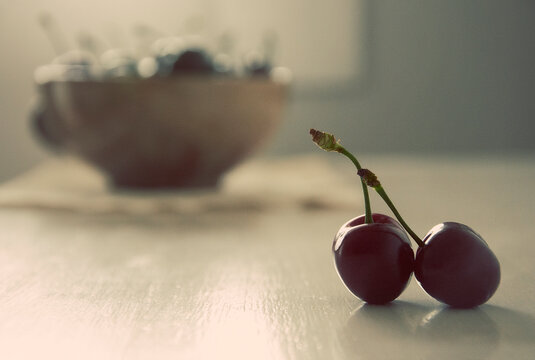 Close-up of to cherries on a table with a bowl of cherries in the background 