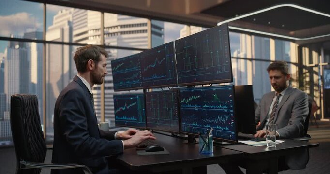 Two Male Brokers Analyze Stock Exchange Data on Multi monitor Desk Setups in Office, Tracking Market Charts. Big Citry Investment Analytics Firm and Capital Growth Startup