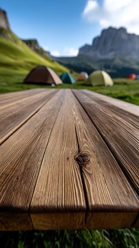 Close up of textured wooden tabletop with blurred tents and green hills in the background under a blue sky