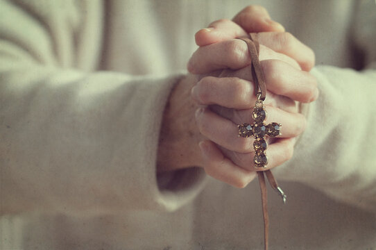 Close-up of a Senior woman with her hands clasped holding a jewelled crucifix