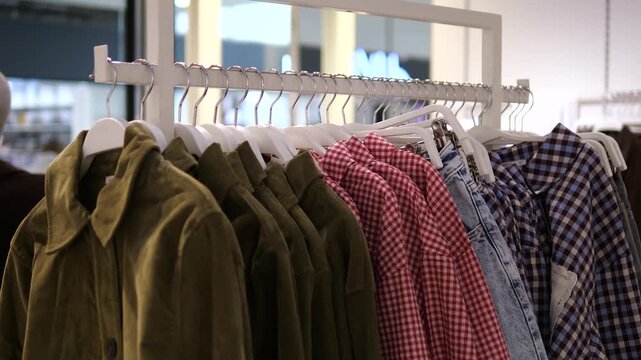 Olive green jackets, red gingham, and blue denim on display. Trendy casual wear hanging on white hangers in a modern boutique. Perfect for autumn fashion marketing and seasonal apparel commercials.